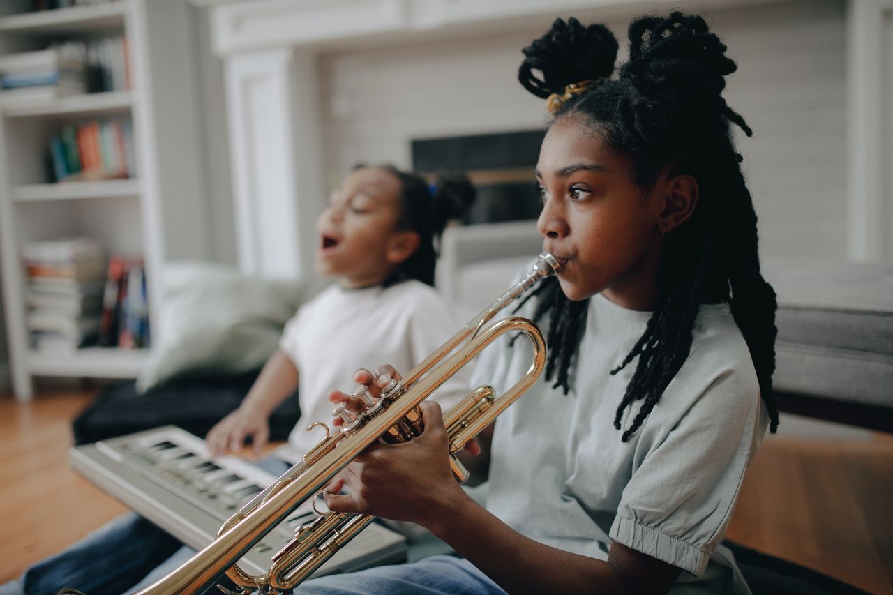 About Girl playing trumpet with sibling at home, enjoying music time.